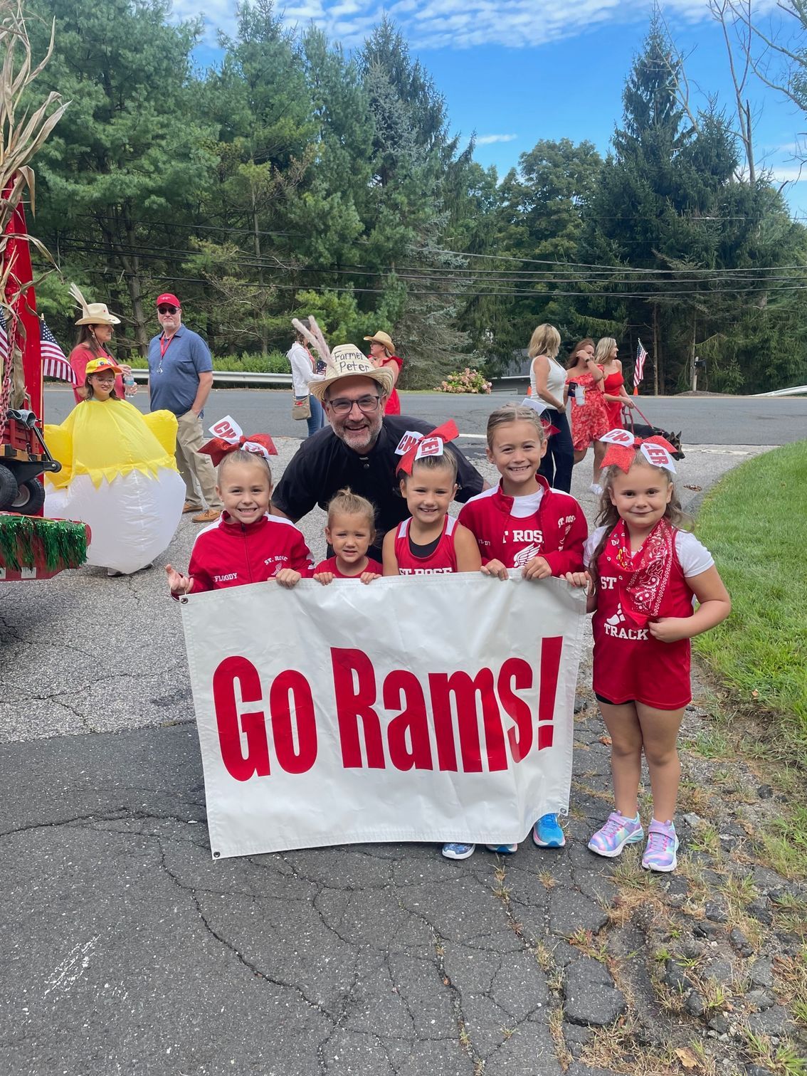 Students and pastor smile as they pose for a photo as they hold a banner that reads Go Rams! as they prepare to march in the Labor Day parade