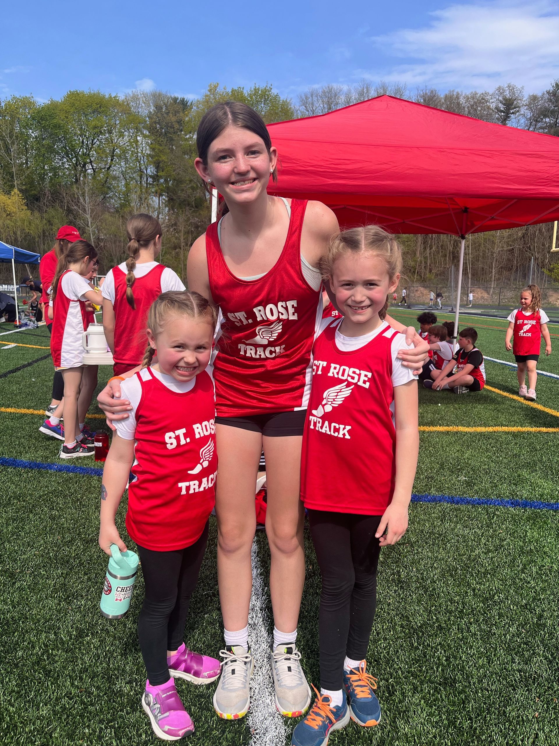 Three female students of varying ages wearing Track uniforms smile for the camera 