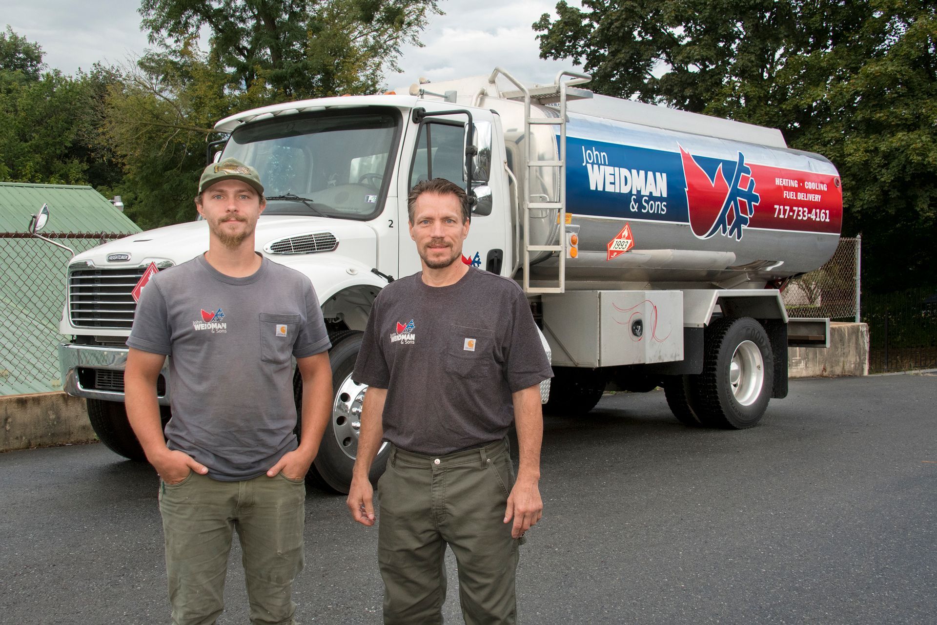 A man in a red shirt is talking to a woman in front of an air conditioner.