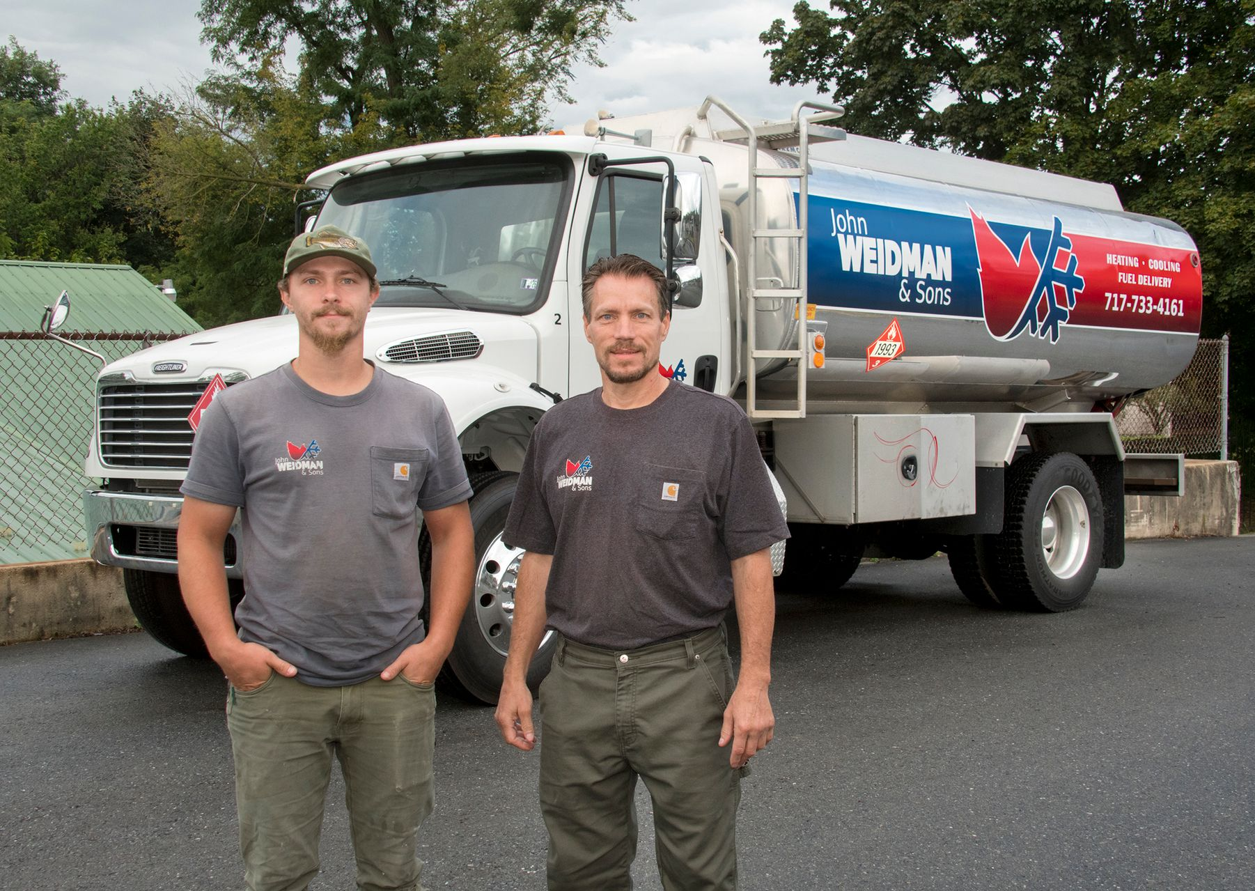 A man in a red shirt is talking to a woman in front of an air conditioner.