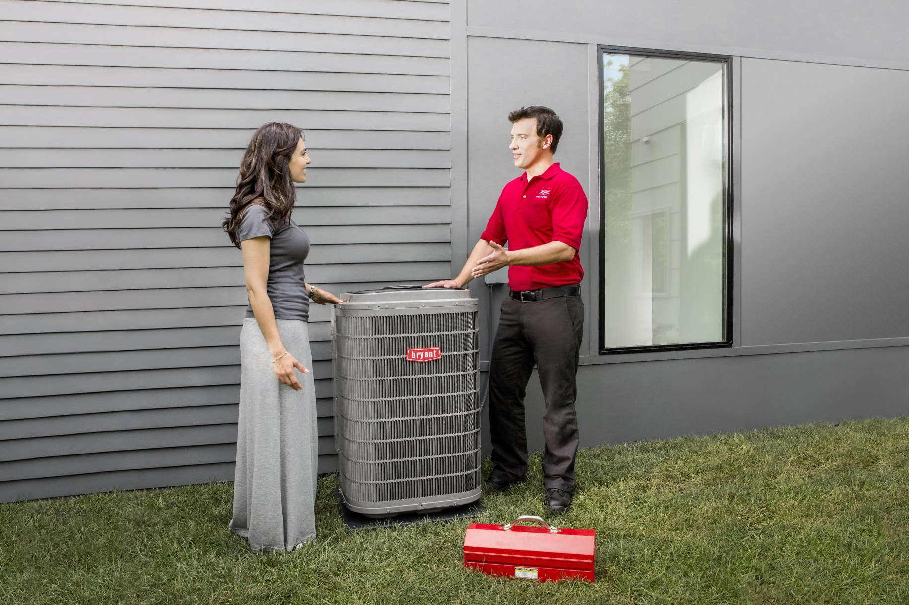 A man in a red shirt is talking to a woman in front of an air conditioner.