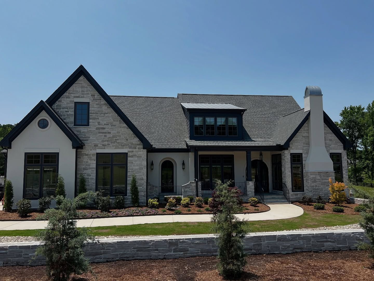Stone and stucco house with dark roof and trim, under a clear blue sky.