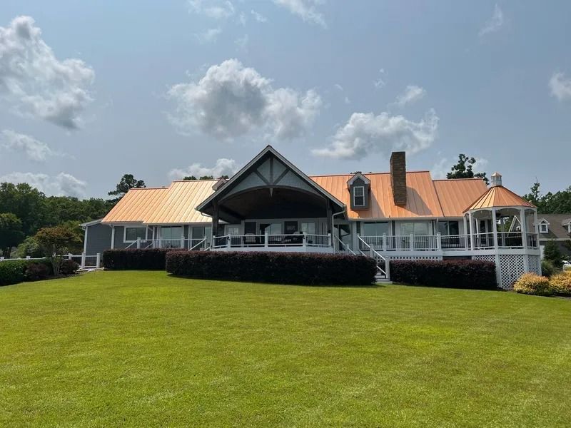 House with copper roof and outdoor patio on a green lawn, under a blue sky with clouds.