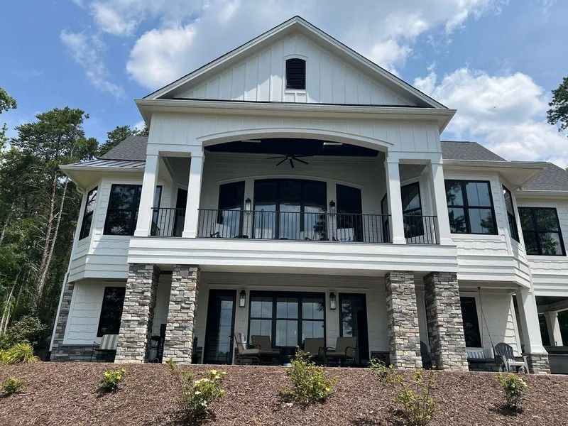 White house with black windows and stone columns, overlooking water on a sunny day.