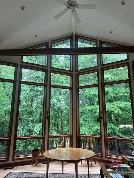 Tall windows with a wooded view; a table and chairs are in the foreground.