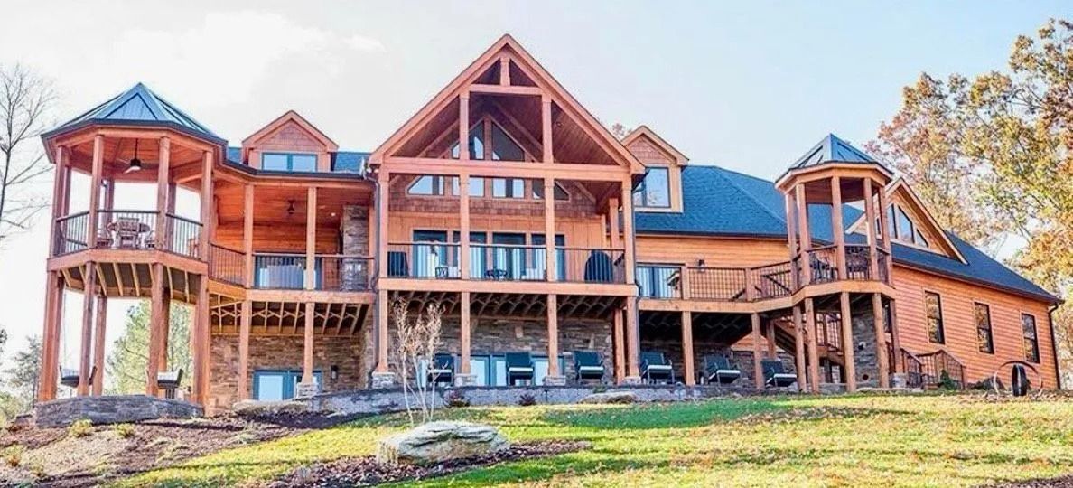 A large wooden house with multiple levels, decks, and turrets sits on a grassy hill.