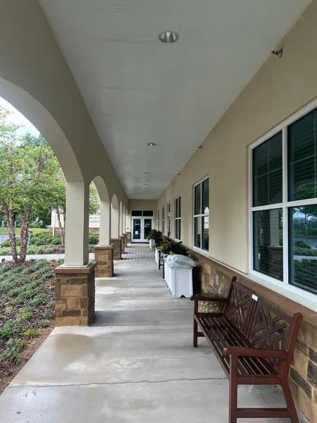 Covered outdoor walkway with columns, windows, bench, and landscaping.