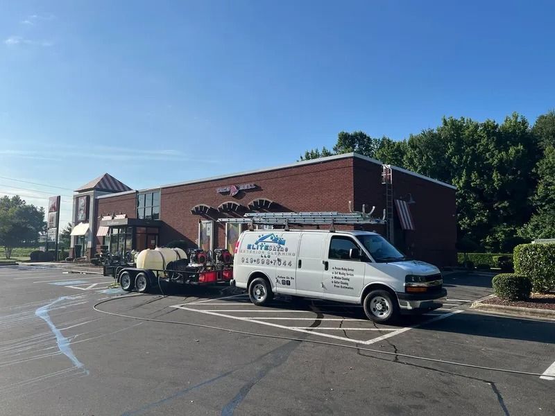 A white van with a trailer parked in front of a brick building. The van has a company logo on the side.