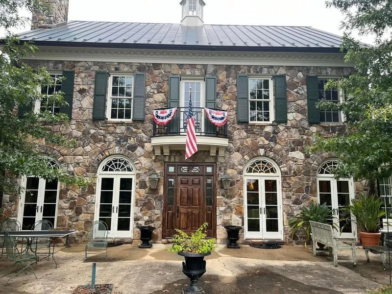 Stone house with dark green shutters, American flag, and double doors.