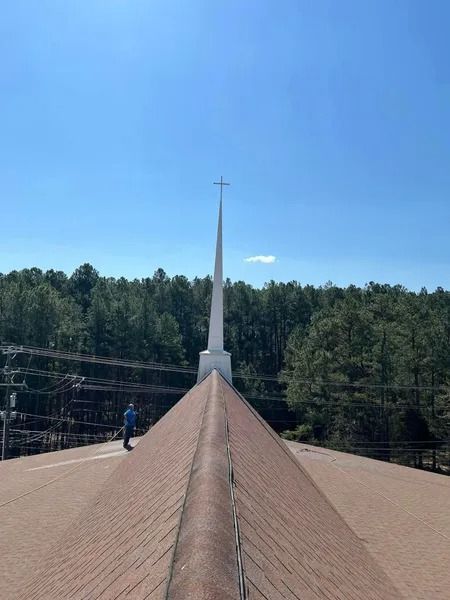Church steeple against a blue sky, roof in foreground, person on roof.