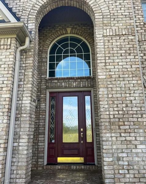 Brick home entrance with arched doorway, large window, and burgundy front door.