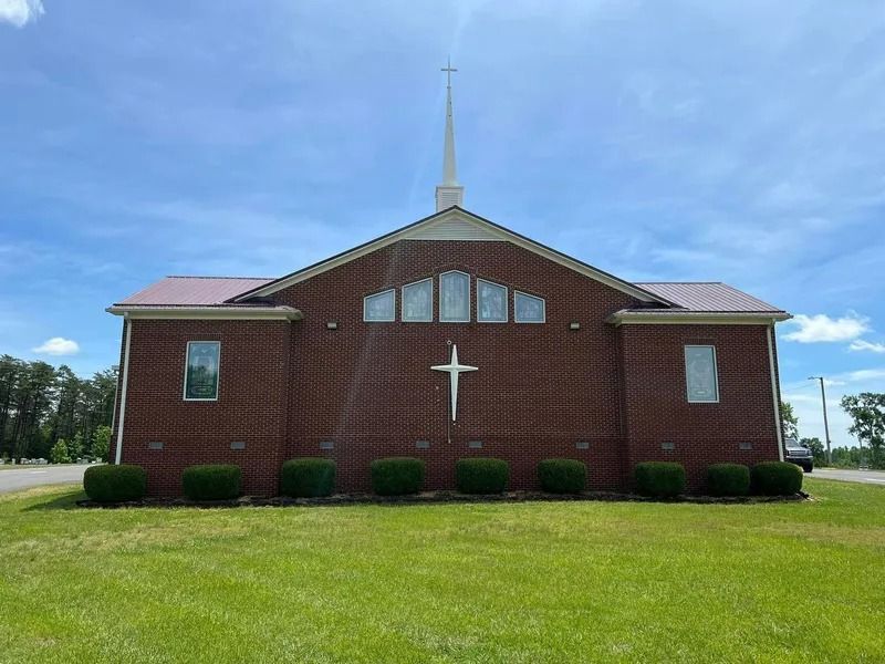 Brick church with white cross, steeple, green grass, and blue sky.