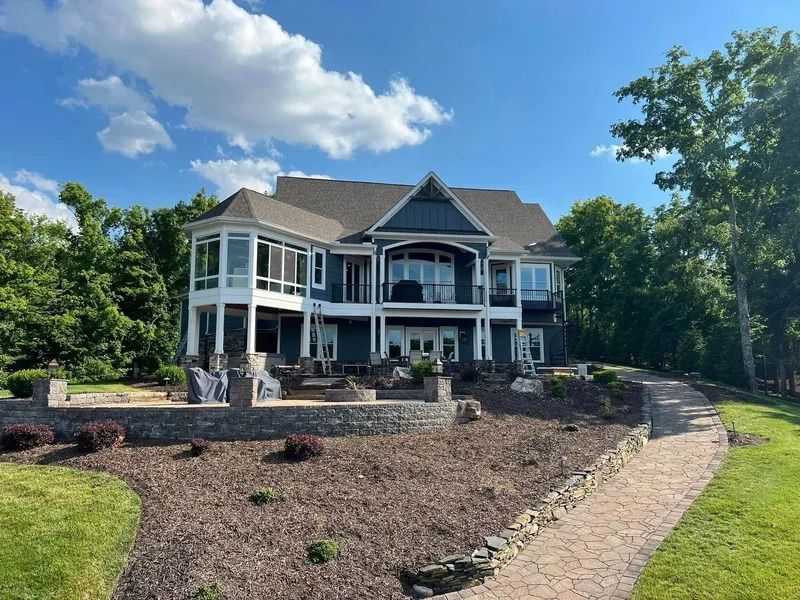 Blue waterfront home with multi-level decks, pathway leading to house, blue sky with clouds.