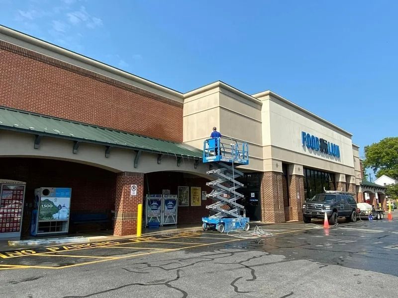 Person on lift washing the exterior of a Food Lion grocery store. Blue sky, brick, and white signage.