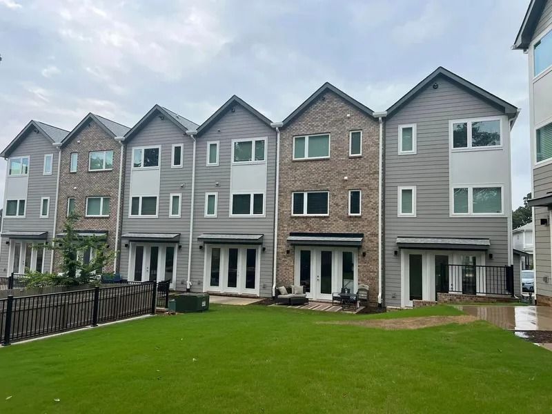 Row of modern townhouses with gray and brick exteriors, French doors, and a green lawn.