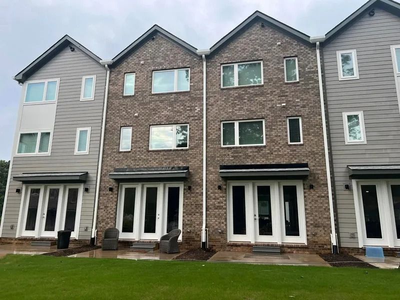 Back view of townhouses with gray siding and brick exteriors, glass doors, and a green lawn.