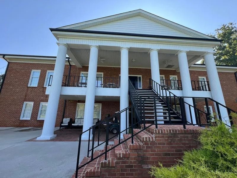 Brick building with white columns and steps. Black railing on the steps, blue sky.