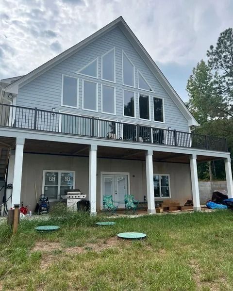 Two-story house with light blue siding, black railing, large windows, and a lower-level deck.