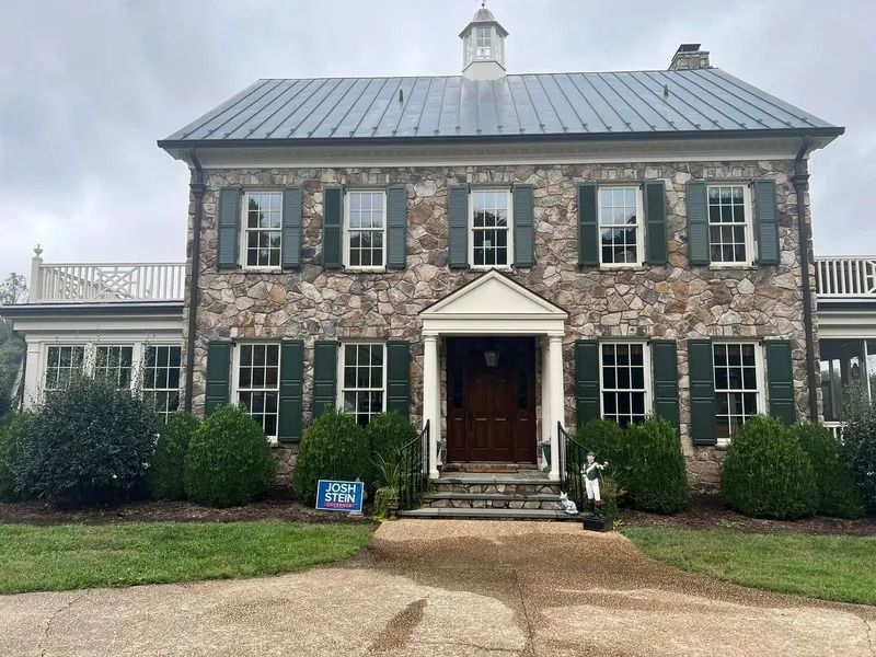 Stone-clad house with green shutters, a metal roof, and a small entry portico. Cloudy sky.