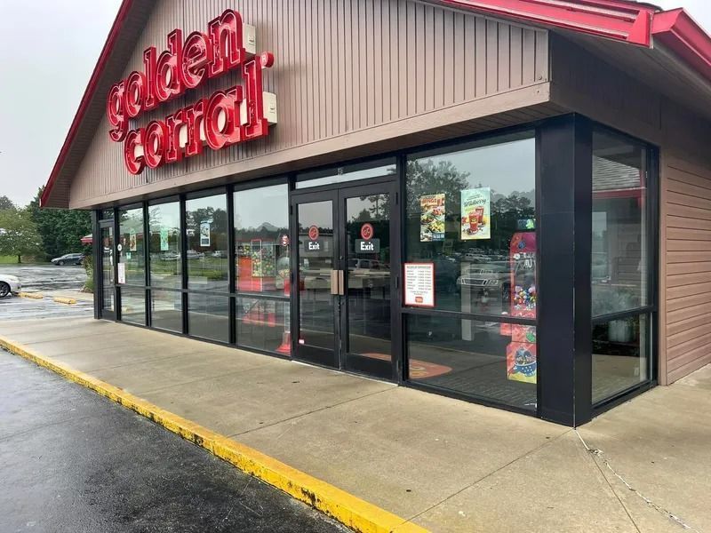 Golden Central store exterior with large windows and red sign. Concrete sidewalk, wet from rain.