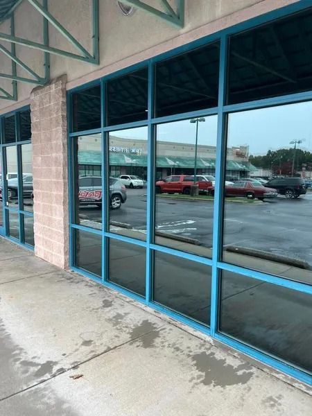 Blue-framed windows reflecting a parking lot with cars and a building, viewed from a sidewalk.