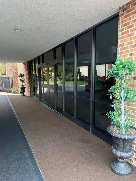 Entrance with glass doors, brick wall, potted plants, and covered walkway.