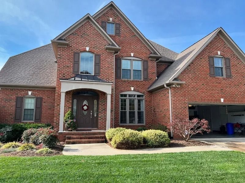 Brick house with brown shutters, door, and roof, green lawn, blue sky.