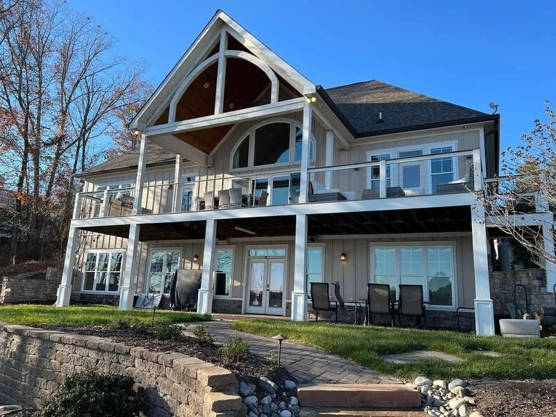 Two-story lakeside home with decks, white trim, and a large arched window.