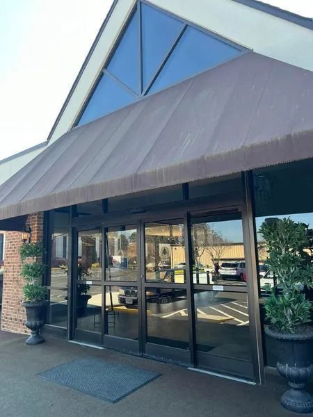 Entrance to a building with brown awning, glass doors, and potted plants.
