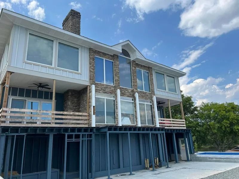 Two-story house with blue siding, stone accents, large windows, and an outdoor deck under a blue sky.