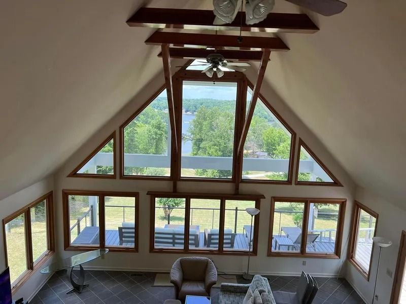Interior view of a room with large windows overlooking a lake. Wooden beams and trim, deck furniture visible.