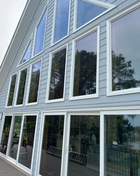 A-frame house with large, white-framed windows reflecting trees and sky. Gray siding.