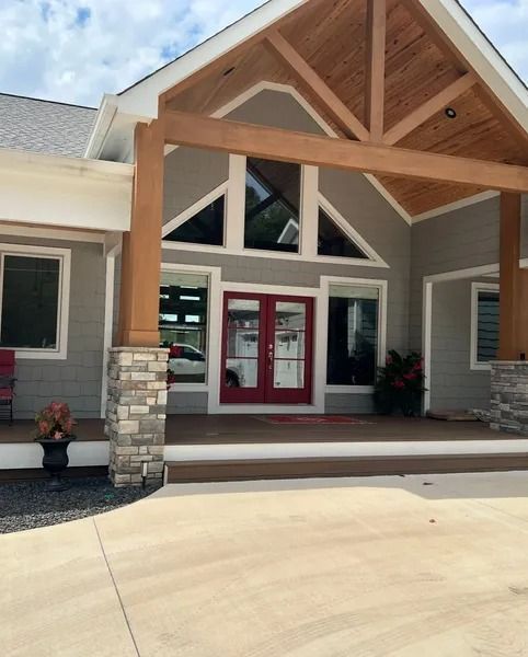 Exterior of a building with red double doors, stone columns, and a covered entryway with wooden beams.
