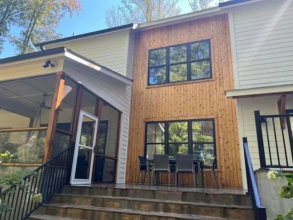 Exterior of a house with light yellow siding, a cedar wood facade, black-framed windows, and a screened-in porch with steps.