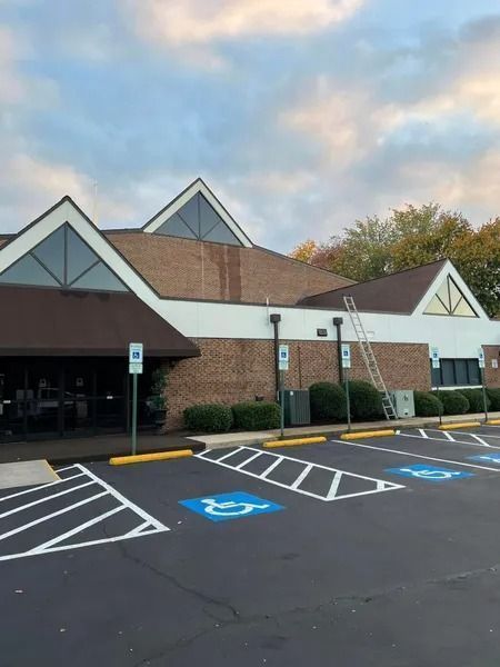 Exterior of a brick building with accessible parking spots marked with blue wheelchair symbols. A ladder leans against the wall.