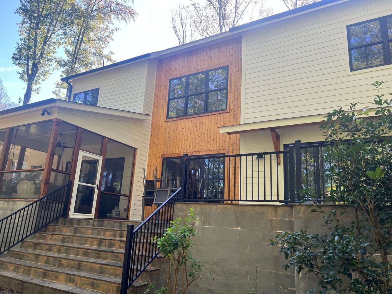 Two-story house with light siding and wood paneling, featuring porch, deck, and stairs.