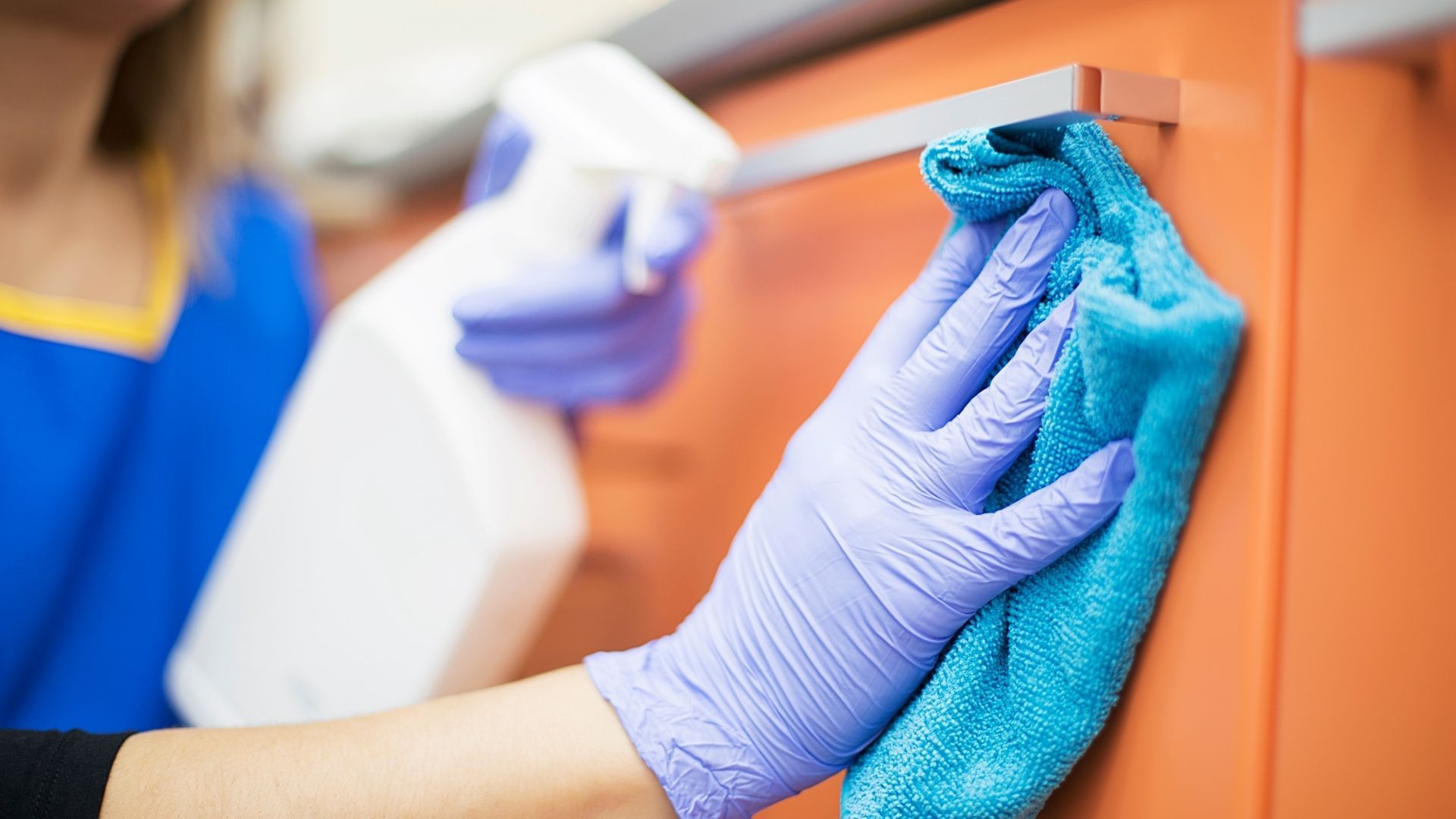 A person wearing purple gloves is cleaning a cabinet with a blue cloth.