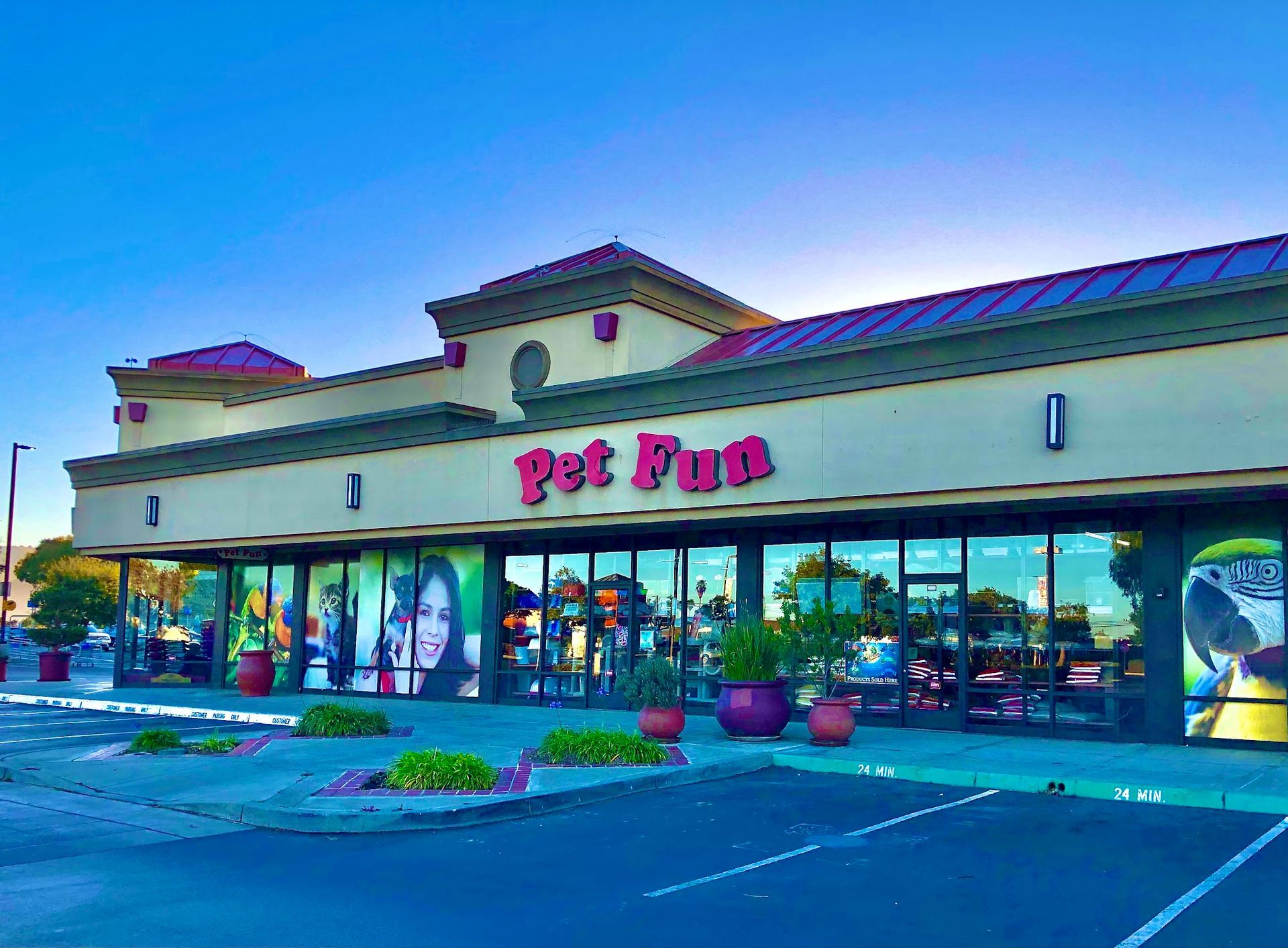 Pet Fun store exterior with window displays, red signage, and potted plants under a blue sky.