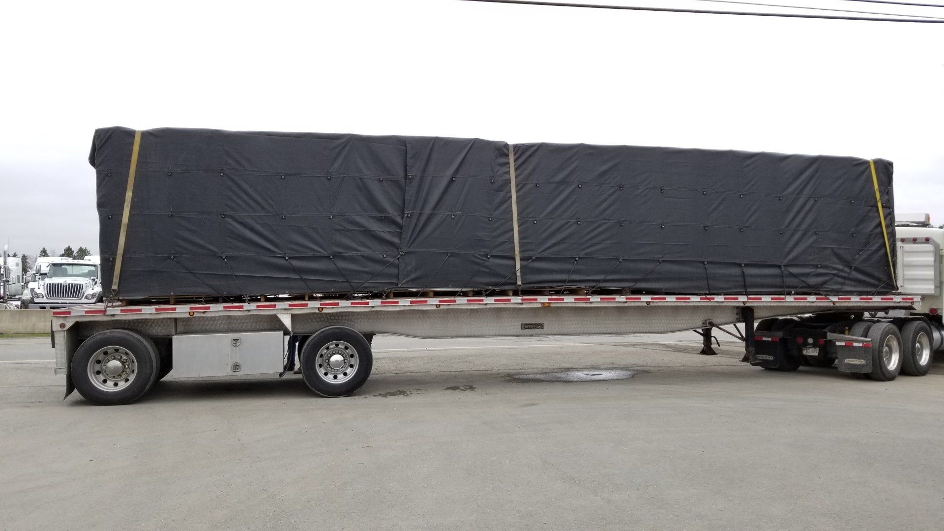 A semi truck with a black tarp on it is parked in a parking lot.