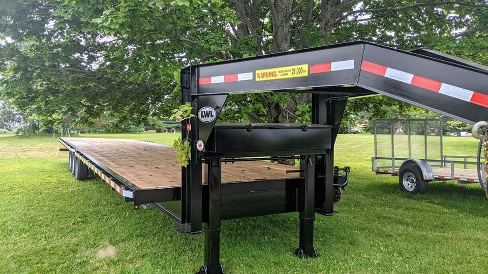 A flatbed trailer with a ramp attached to it is parked in a grassy field.