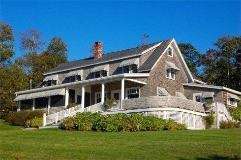 A large house with a large porch sits in the middle of a lush green field