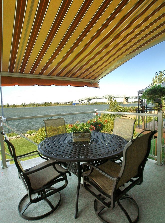 A patio with a table and chairs under an awning overlooking a body of water
