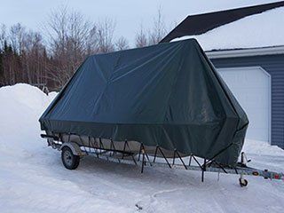A boat on a trailer is covered in a green tarp.