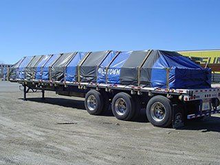 A row of flatbed trailers are parked in a dirt lot
