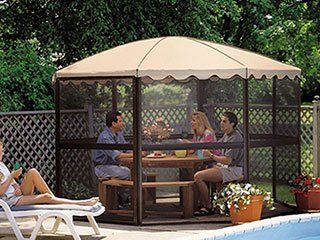 A group of people are sitting under a screened in gazebo near a pool