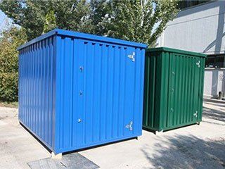 Two blue and green containers are sitting next to each other in a parking lot.