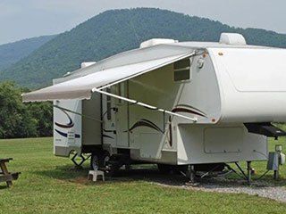 A white rv with an awning is parked in a grassy field with mountains in the background.