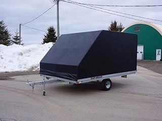 A black trailer is parked in front of a green building.
