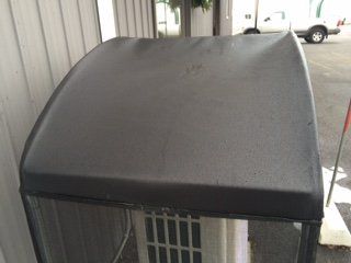 A black canopy is sitting on top of a white air conditioner.