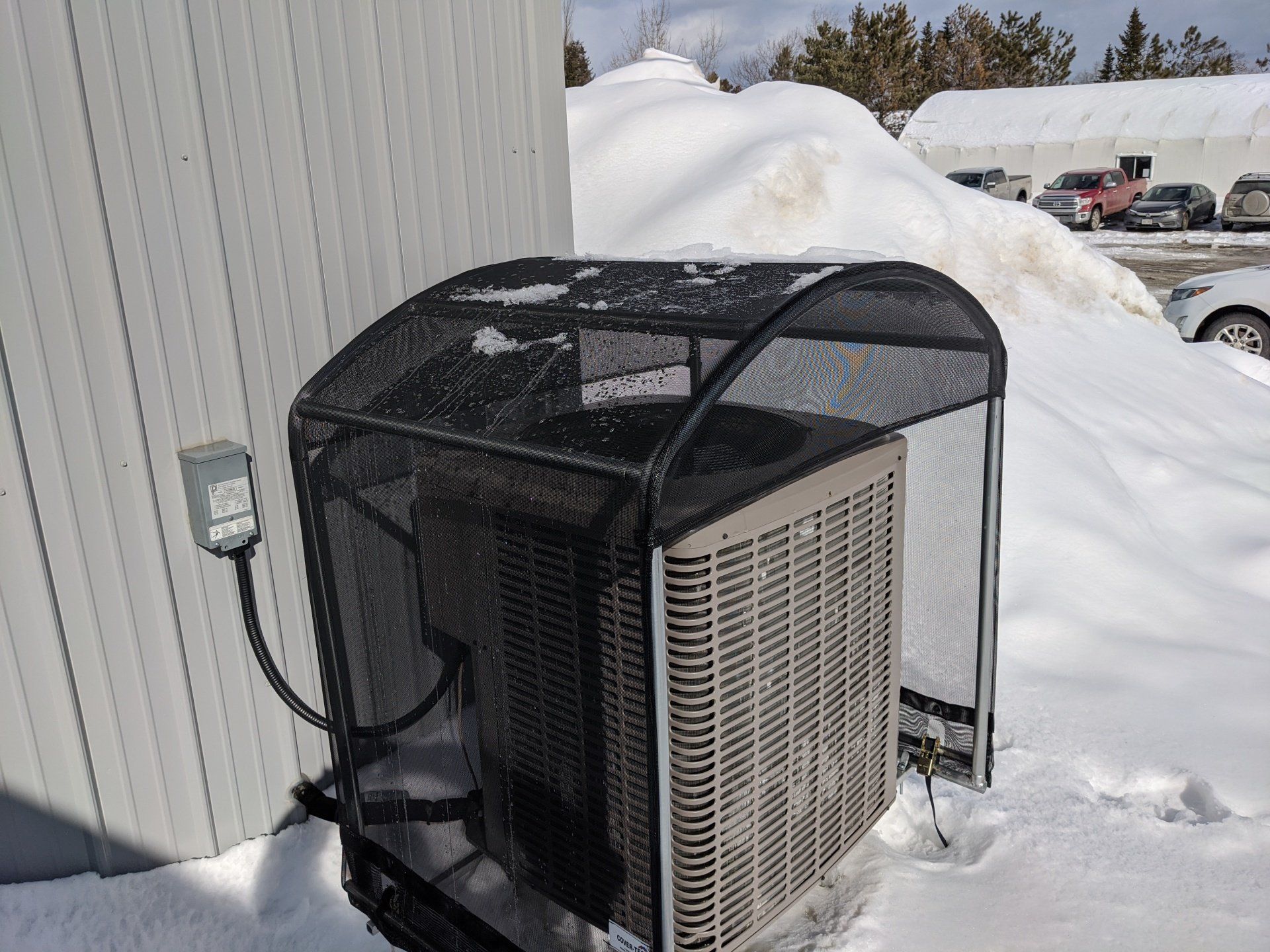 An air conditioner with a cover on it is sitting in the snow.